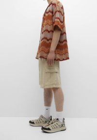 Chemise en tricot à manches courtes avec motif en zigzag dans des tons chauds, associée à un short cargo beige avec de grandes poches latérales et des baskets à cheville.