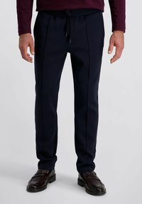 Navyblauwe op maat gemaakte broeken met een elastische taille, voorzien van gestikte naden en een gladde textuur, in combinatie met donkere leren loafers.