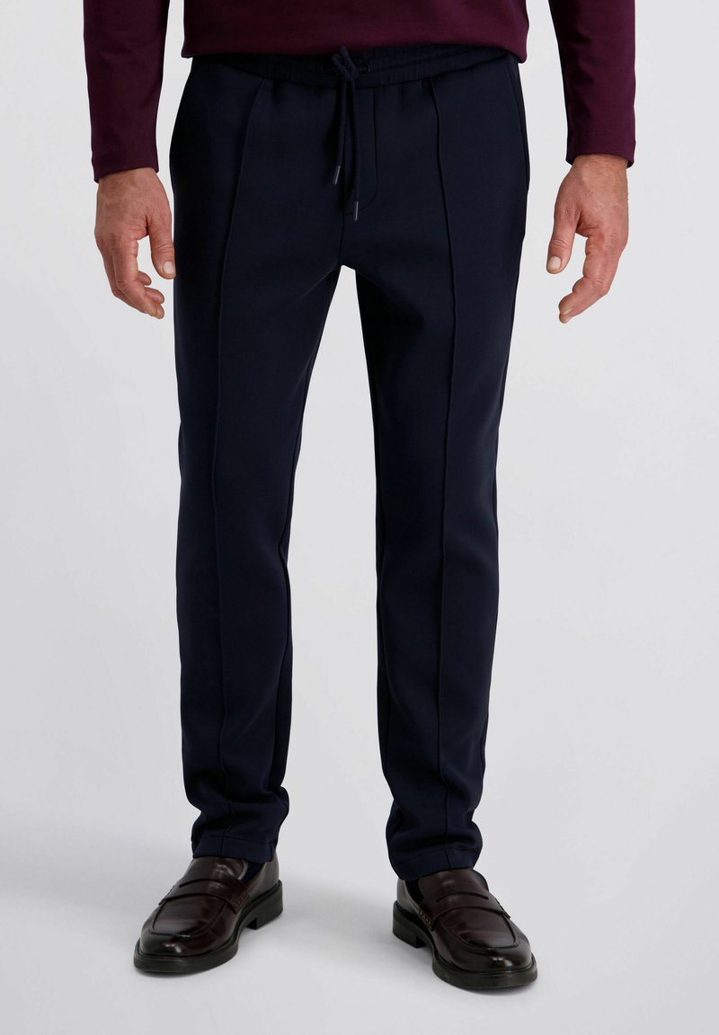 Navyblauwe op maat gemaakte broeken met een elastische taille, voorzien van gestikte naden en een gladde textuur, in combinatie met donkere leren loafers.