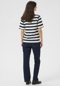 Dryžuota t-shirt tamsiai mėlynos ir baltos spalvų, trumpomis rankovėmis, derinama su tamsiai mėlynomis džinsomis ir juodais batais, matoma iš nugaros.