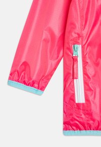 Rožinė vandeniui atspari striukė su blizgiu paviršiumi, turinti turkišo spalvos užtrauktuką, kišenę ir rankogalius, taip pat subtilų tinklo raštą medžiagoje.