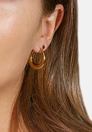 Gold hoop earrings with a smooth, shiny finish, featuring a smaller gold stud earring. Both have a minimalist design and subtle texture.