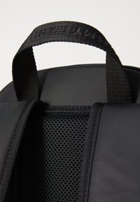 Black backpack featuring a textured mesh panel, sturdy straps, and a reinforced handle for durability and comfort.