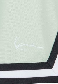 Maillot de sport vert menthe clair avec tissu mesh respirant, présentant des rayures noires et blanches ainsi qu'un logo brodé blanc à l'ourlet.