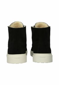 Botines de ante negro con suela de goma blanca y un acogedor forro beige. Presentan un diseño sencillo sin embellecimientos adicionales.