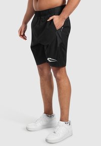 Svarta träningstights med elastisk midja, sidofickor och en kontrasterande panel. Visas med vita sneakers.