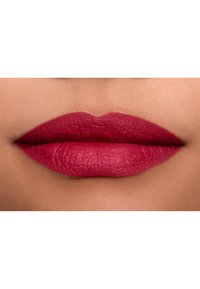 Couleur à lèvres matte dans une teinte de baies foncées, avec une texture lisse et des bords bien définis, contrastée par un fond de teint neutre.