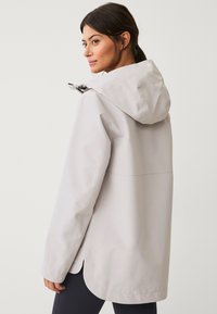 Hellgraue wasserdichte Jacke mit verstellbarem Kapuze, seitlichen Schlitzen und langen Ärmeln. Glatte Textur und minimalistische Designdetails.