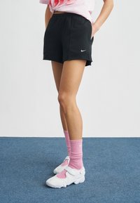 Μαύρο αθλητικό σορτς με ελαστική μέση, πλαϊνές τσέπες και μικρό λευκό λογότυπο. Συνδυασμένο με ροζ ριμπ καλτσάκια και λευκά αθλητικά παπούτσια.