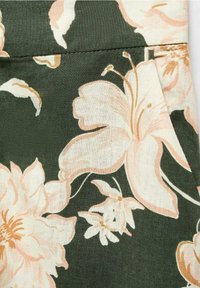 Tissu vert foncé avec grand imprimé floral pêche pâle et crème, montrant une couture et un détail de bord cousus.