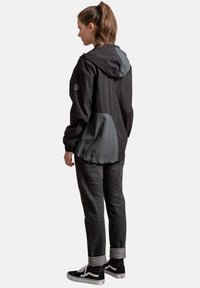 Zwarte hoodie-jack met grijze accenten, gemaakt van lichtgewicht stof, heeft een ruime pasvorm en een longitudinale naad aan de achterkant. Gecombineerd met donkere jeans en sneakers.