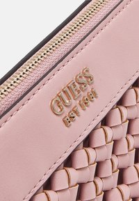 Lyserød læder clutch med vævet tekstur, guld lynlås og præget "GUESS EST 1981" logo. Der er glatte og blanke accenter.