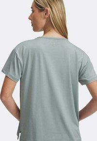 Camiseta de manga corta verde claro con textura suave, escote redondeado y aberturas laterales para mayor comodidad. Logo visible en la parte posterior.