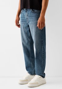 Ljusblå denimjeans med lös passform och klassisk design med fem fickor. Bärs med vita sneakers och visar strukturerat tyg.