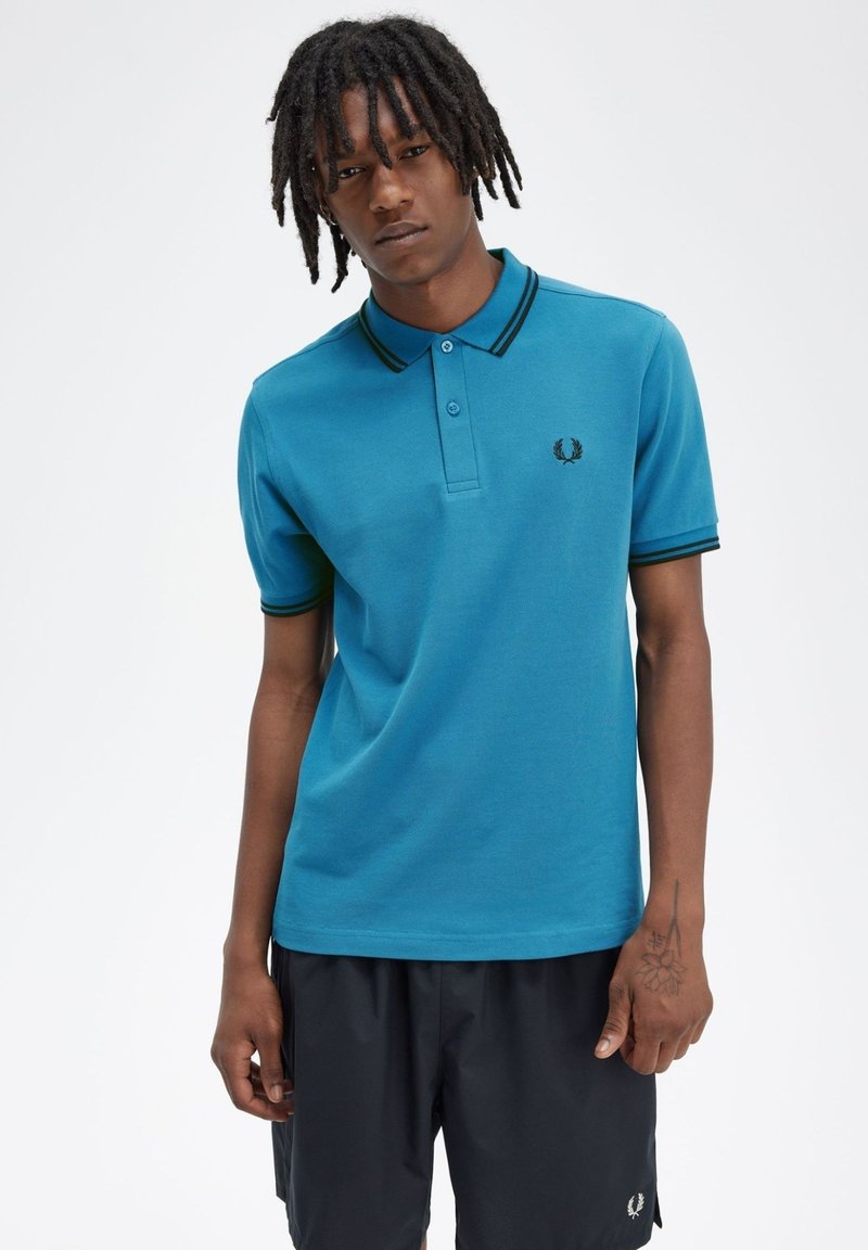 Polo shirt turchese con colletto classico, dettagli neri sul colletto e sulle maniche, con un piccolo logo sul petto.