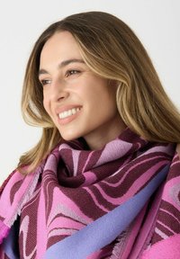 Écharpe multicolore arborant de forts motifs abstraits en rose, violet et bordeaux. Fabriquée en tissu texturé avec des bords à franges.