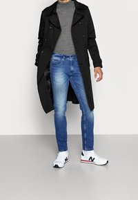 Černý trenčkot, šedý rolák, modré džíny, bílé tenisky New Balance s červenými a námořnickými detaily. Hladká látka a přiléhavý střih.