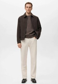 Chaqueta marrón oscuro con cremallera, suéter marrón texturizado, pantalones crema y zapatos negros. El conjunto presenta un diseño minimalista con colores neutros.