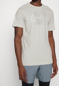 Jasnobeżowa koszulka z krótkim rękawem wykonana z bawełny, z teksturowanym białym logo Nike na przodzie.