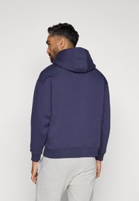 Sudadera con capucha de color navy, con una gran capucha, puños y dobladillo acanalados, tela suave y un diseño sencillo. Llevada con pantalones de chándal gris claro.