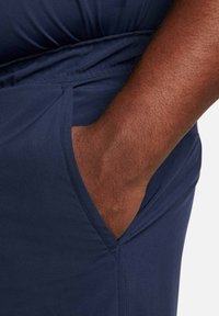 Navy fabric with a smooth texture. Close-up of a hand resting in a side pocket of a garment, showing stitching details and fit.