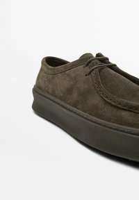 Chaussure en daim vert foncé avec un orteil arrondi, deux œillets en haut et une épaisse semelle en caoutchouc noir. Dispose de détails de couture subtils le long du bord.