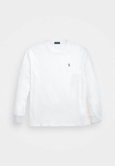 Hosszú ujjú, fehér póló, pamutból készült. Kerek nyakkivágása van, és egy kis, hímzett logó található a mellkasán. Simább textúrájú.