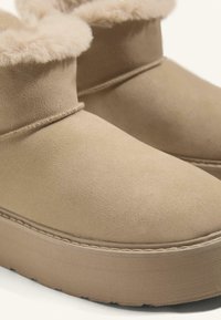 Bež čizme do gležnja od mekog nubuka s krznom na rubu. Debeli đon s detaljima šivanja i zaobljenim vrhom.