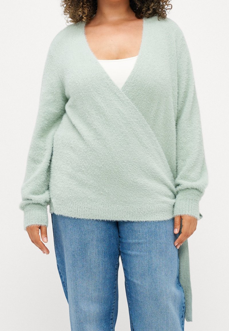 Mjukt, ljusgrönt omslagströja med långa ärmar och djup V-ringning. Har strukturerad stickning och sidodetaljer som sträcker sig nedanför midjan.