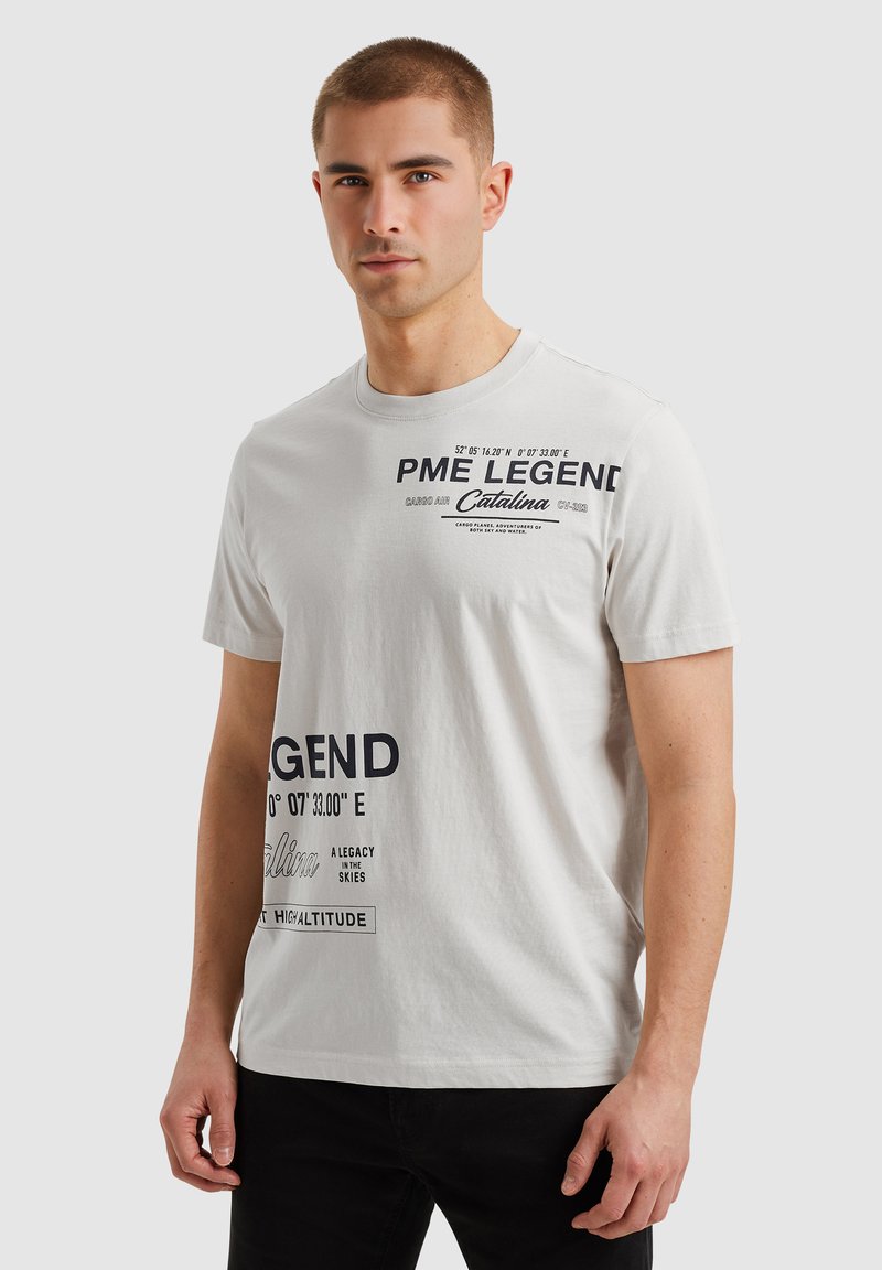Camiseta de algodón blanca con gráficos de texto en color navy, cuello redondo y mangas cortas. Muestra de manera prominente las coordenadas geográficas y el nombre de la marca.