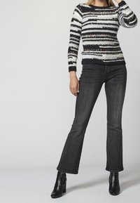 Knitted black and white striped sweater with metallic accents, paired with flared black denim jeans and black ankle boots.