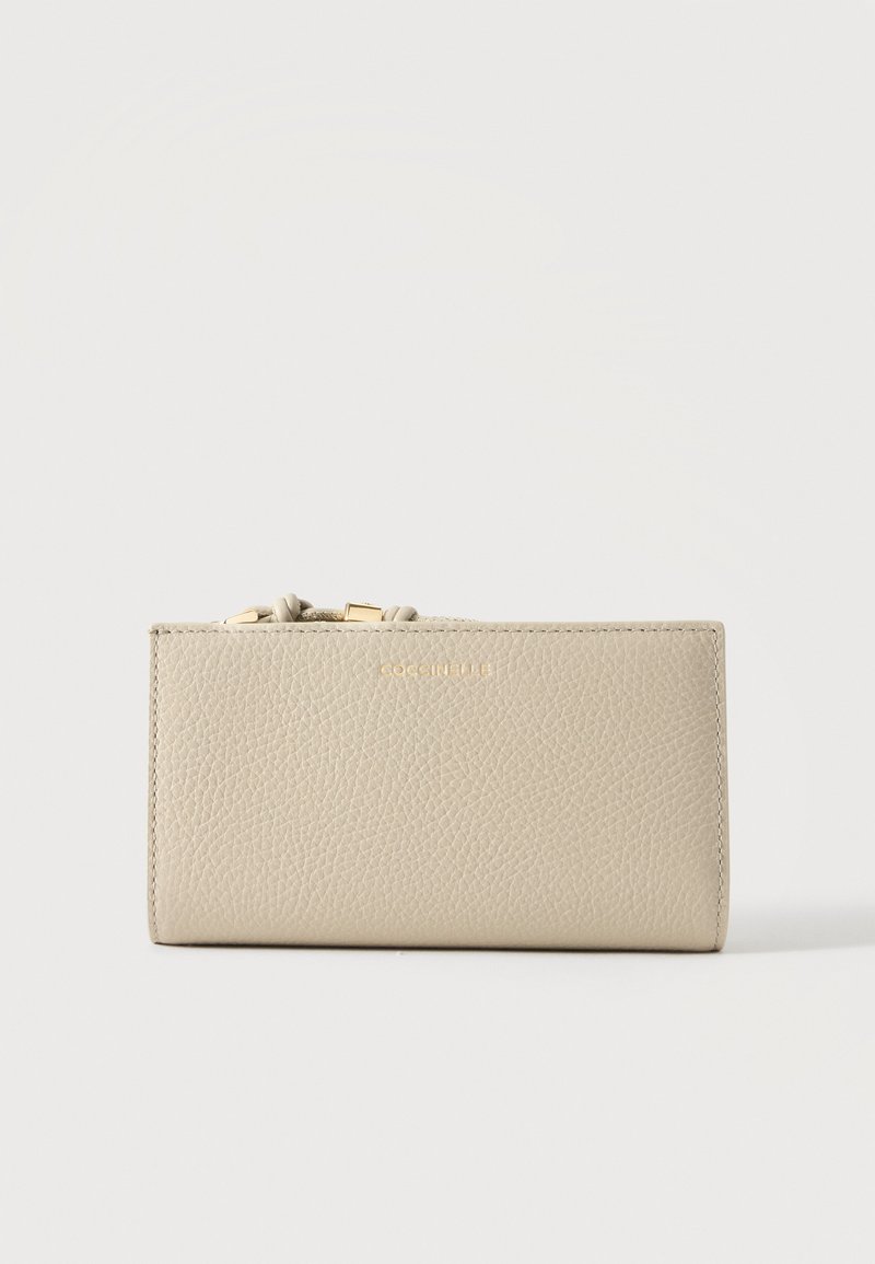 Portefeuille en cuir texturé beige avec fermeture éclair dorée et petit nom de marque embossé « Coccinelle » au centre devant.