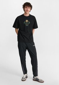 Czarny bawełniany t-shirt z grafiką z przodu, w połączeniu z czarnymi spodniami dresowymi z szarymi akcentami i elastycznymi mankietami. Dopełnieniem są codzienne buty.