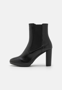Bota de tornozelo em couro preto com um salto robusto, apresentando painéis laterais elásticos e um acabamento suave e brilhante. Bico arredondado com um design minimalista.