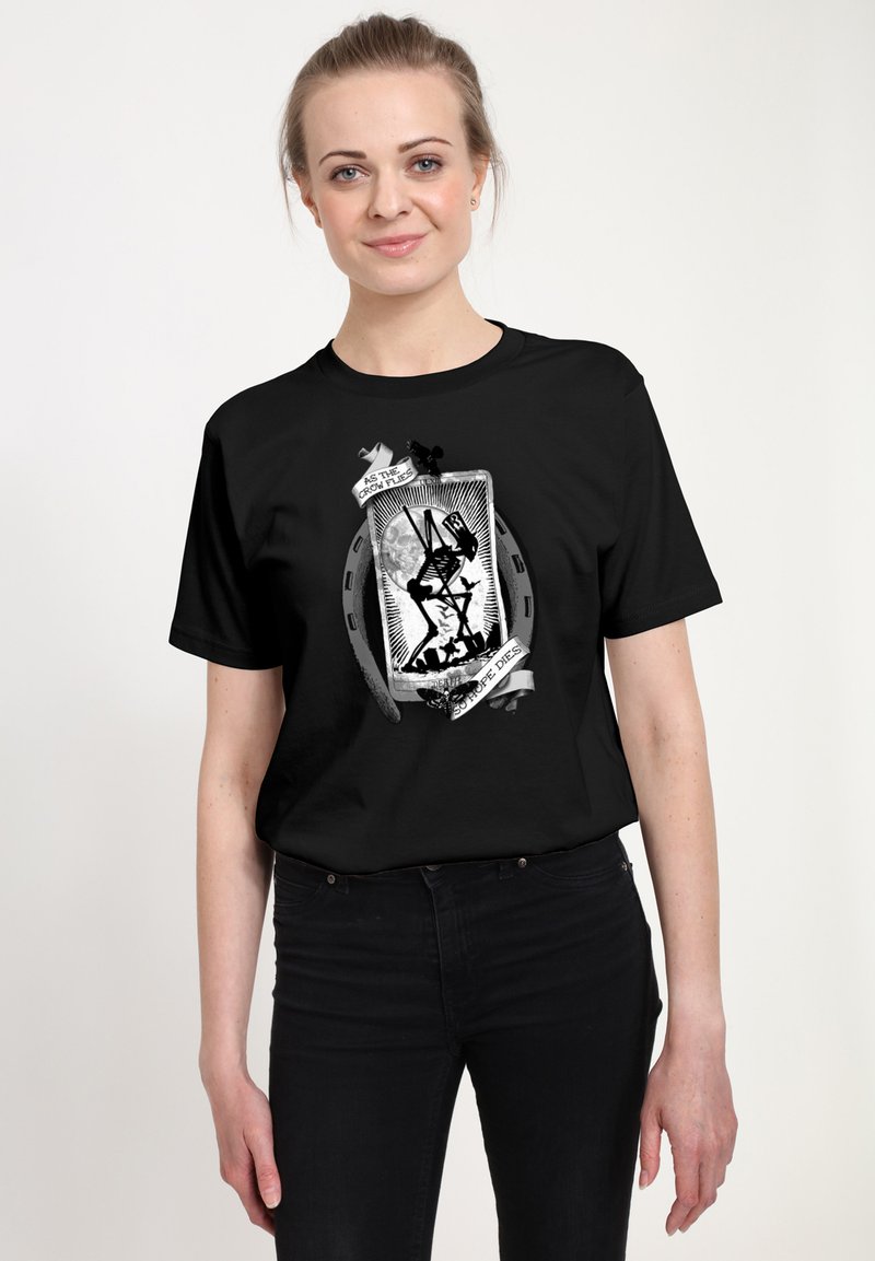Woman wearing black t-shirt featuring skeleton with scythe inside horseshoe and ribbon reading "As the crow flies, so hope dies."