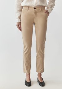 Beige Hosen aus glattem Stoff mit geradem Schnitt, ausgestattet mit Vorderhosen taschen und einem einzigen Knopfverschluss an der Taille.