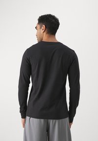 Black long-sleeve shirt in soft fabric with a round neck, featuring a simple design and a slightly fitted silhouette.