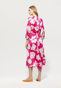 Blumenkleid in Pink mit weißen Blumen, mit 3/4-Ballonärmeln und einer Länge bis zur Mitte der Waden. Kombiniert mit orangefarbenen Slippern.