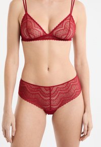 Bralette de encaje rojo con borde festoneado, con tirantes delgados y ajustables, y braguitas de encaje rojo a juego con estilo festoneado y corte de talle medio.