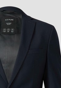 Marineblaues Blazer mit Reverskragen, einreihiger Knopfverschluss und einer Brusttasche. Innenetikett enthält Pflegehinweise und Informationen zum Stoff.