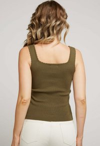 Débardeur côtelé vert olive avec des bords festonnés, coupe ajustée et bretelles étroites. Texture lisse et silhouette simple et classique.