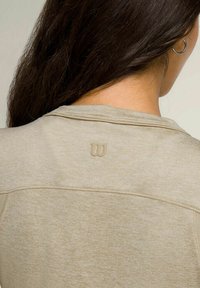 Maglietta sportiva beige con una sottile texture, scollo rotondo e un piccolo logo in rilievo sulla parte superiore della schiena.