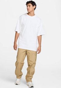 Camiseta blanca de gran tamaño con mangas cortas y un pequeño logo en el pecho, combinada con pantalones cargo beige que cuentan con bolsillos laterales.