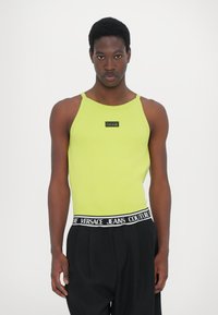 Grønn ribbet tanktop med en svart logopatch, kombinert med svarte bukser med en merkebasert elastisk midje. Enkelt og tettsittende design.