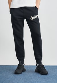 Melnas sporta bikses ar elastīgām aprocēm un kabatām, ar baltu un zelta izšūtu Nike logotipu kreisajā augšstilbā.