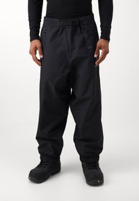 Crne, vodootporne hlače sa elastičnim pojasom, podesivim remenom i patentnim zatvaračem. S manžetama na gležnjevima i glatkom, mat teksturom.