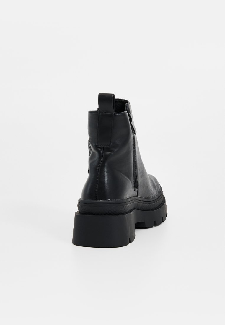 Stivali alla caviglia in pelle nera con suola spessa, zip posteriore e linguetta sul retro, caratterizzati da una texture liscia e un design a punta arrotondata.