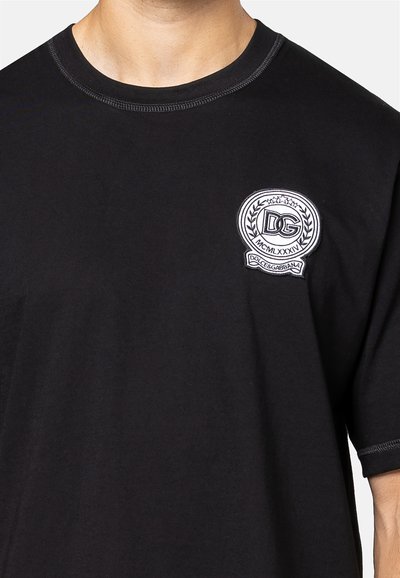 Zwarte katoenen t-shirt met een ronde halslijn, voorzien van een geborduurd wit logo en decoratieve accenten op de borst.