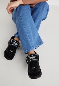 Svarta kviltade skor med tjock sula och kardborreband, med "Buffalo"-märke och vit sömnad, i kombination med blå utsvängda jeans.