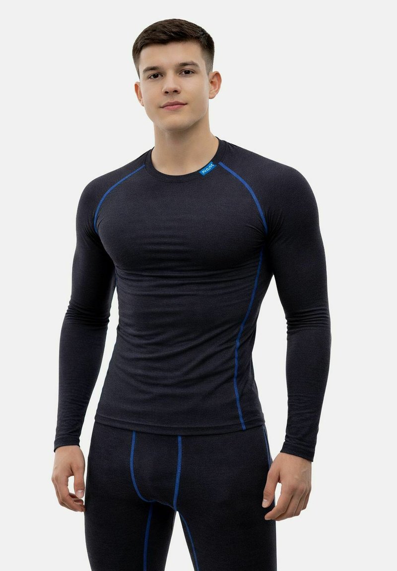 Junger Mann trägt ein enganliegendes schwarzes Langarm-Thermooberteil und passende Hosen mit blauen Nahtakzenten, steht vor weißem Hintergrund.